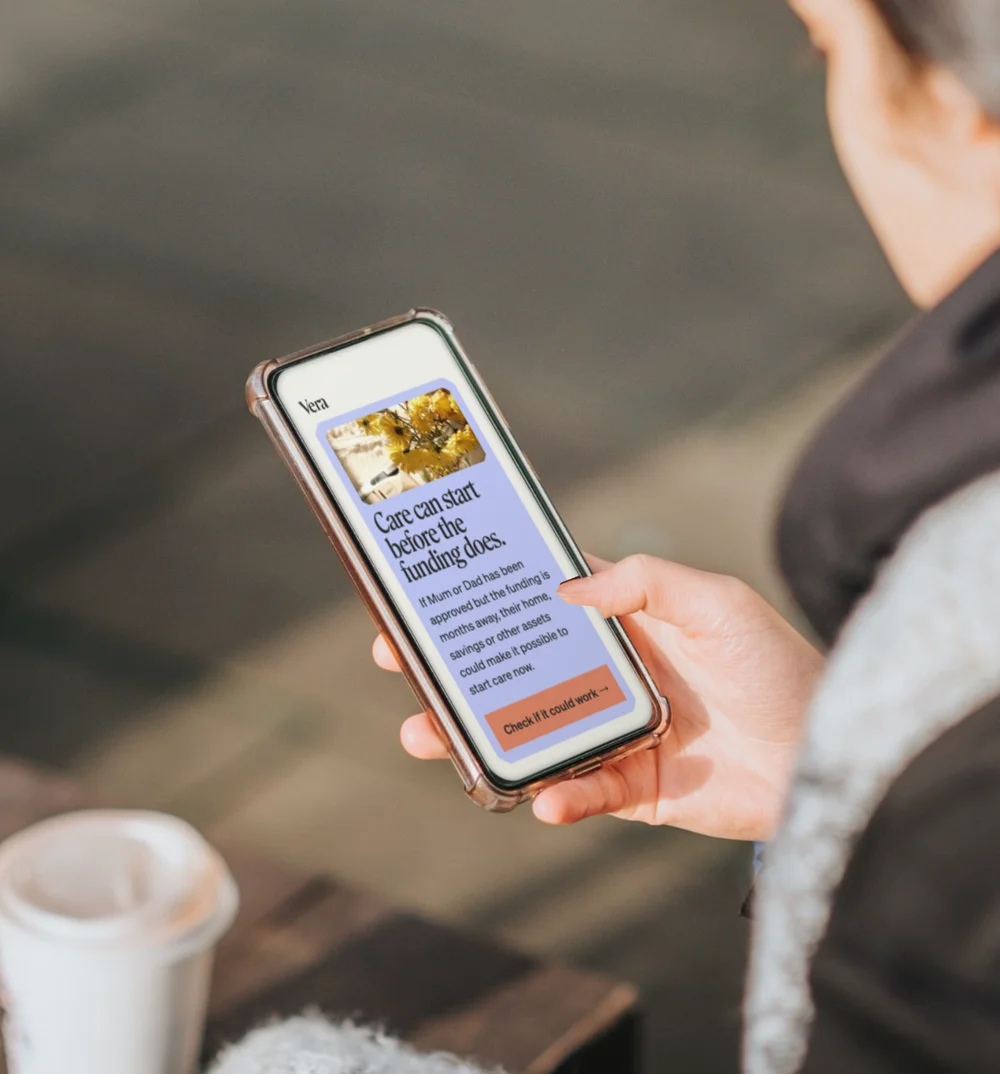 A person holding a phone showing Vera’s care guidance, with a takeaway coffee beside them